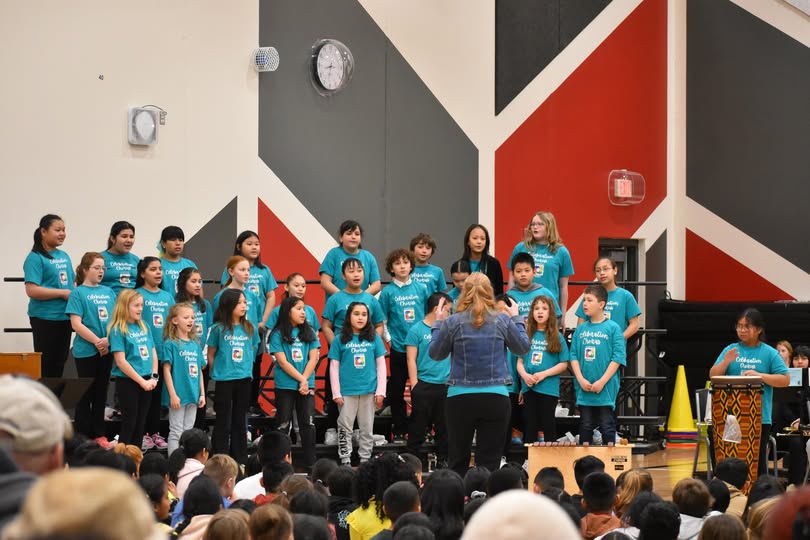 Students singing on risers led by Ms. Mow and accompanied by student on a drum