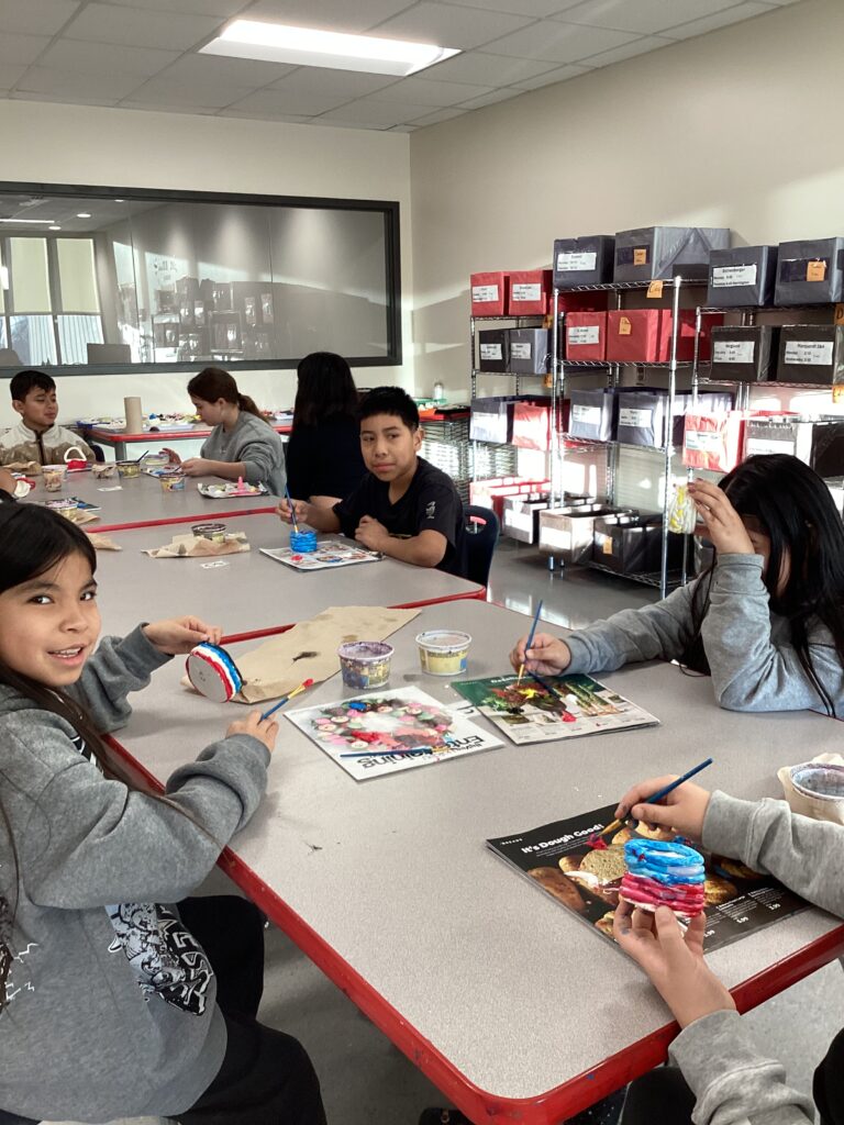 4 students sitting at tables painting