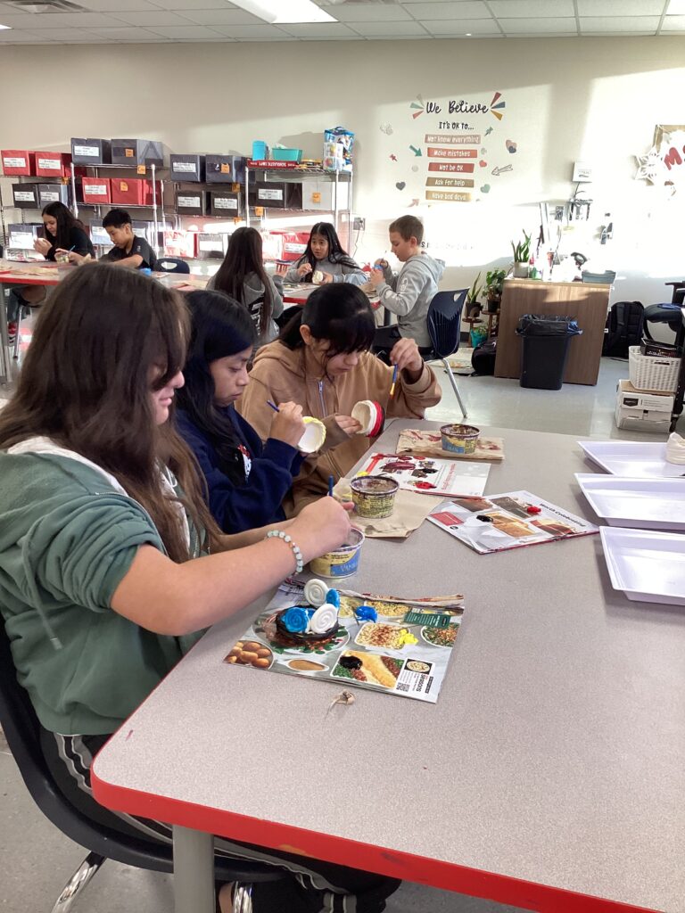 3 students in the foreground painting with other students in the background